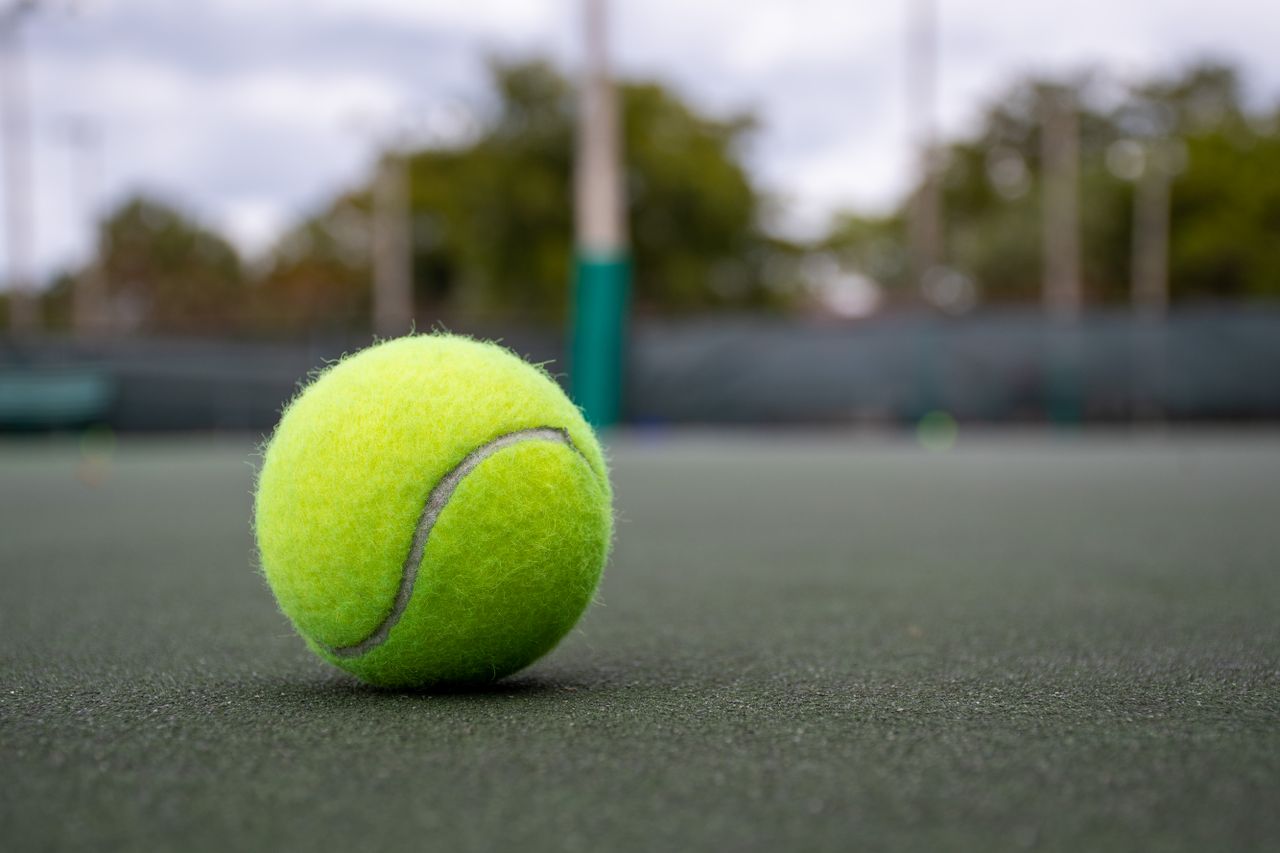 Vibrant tennis ball on outdoor court surface, focusing on texture and color.